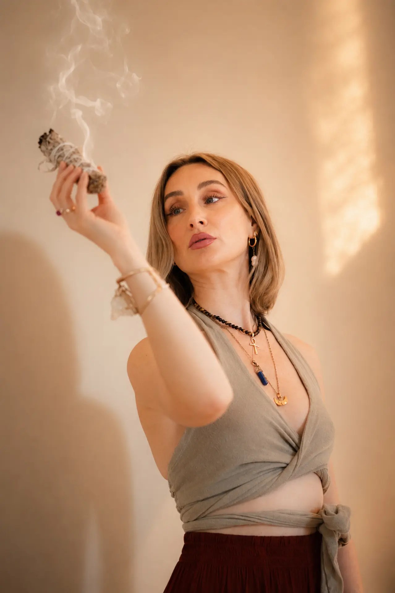 Monika holding a burning sage stick at eye level, smoke rising in warm light